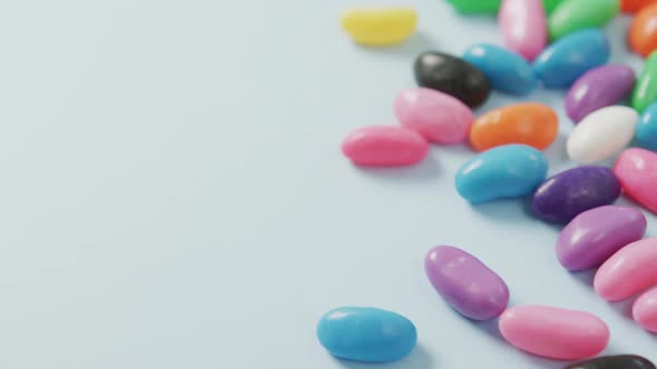 Video of overhead view of multi coloured sweets with copy space over blue background