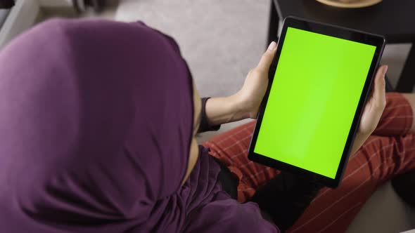 A Muslim Woman Looks at a Tablet (Vertical) with Green Screen in an Apartment  Top Closeup