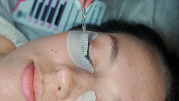 Eyelash Extension Master Combs the Extended Eyelashes on the Eye of a Beautiful Woman with a Brush