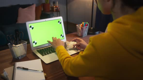 Beautiful Black Woman Sitting at Her Desk Works on a Laptop with Green Chroma Key Mockup Screen