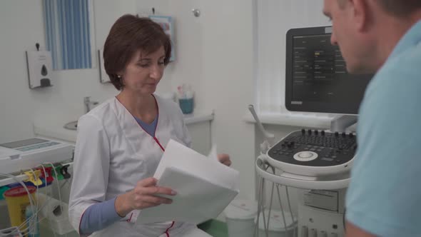 Female Doctor Consults Male Patient Holding Test Results in Hands in Office of Clinic