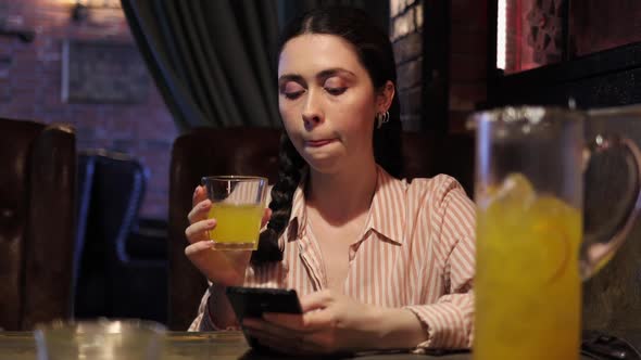 Young pretty caucasian woman drinks a non-alcoholic mocktail and uses a smartphone