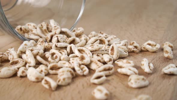 Uncooked wheat flakes scatter on a board from a glass cup