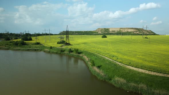 Blooming rapeseed field. On the edge of the field there is a pond. A mothballed city dump is visible