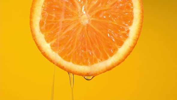 Natural oil flows down from orange on yellow background. Orange slice and water splashing, drops