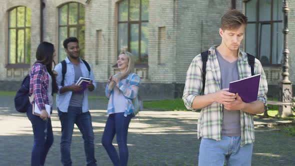 Lonely Male Student Looking at Happy Laughing Classmates Standing Near College