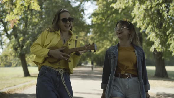 Portrait Two Relaxed Joyful Female Hippies Sunglasses Walking Outdoors Sunlight Playing Ukulele