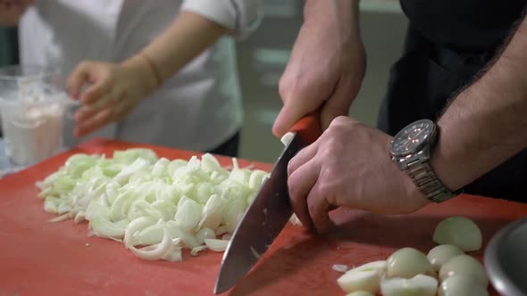 Chef Chopping a Red Onion with a Knife on the Cutting Board in Restaurant Kitchen