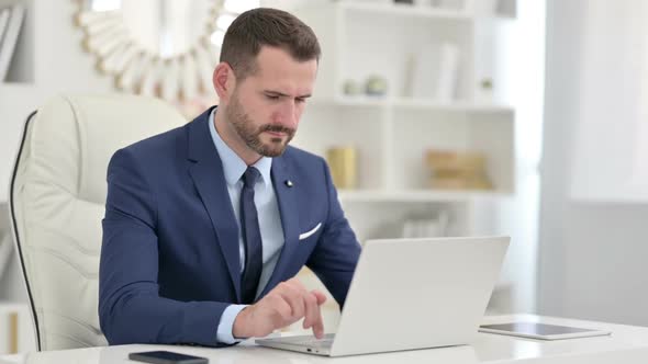 Businessman with Laptop Having Neck Pain in Office