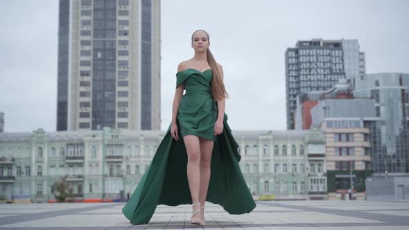 Beautiful Gorgeous Girl in a Stunning Evening Green Dress Walking Fascinatingly on Empty City Square