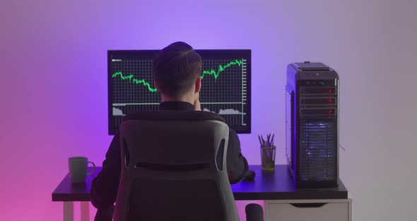 Rear View of Man Trading Stock Market on Pc Computer at Night Room Filled Neon Light