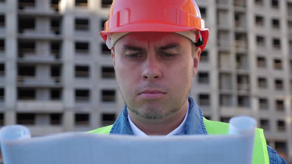 Engineer with Blueprint in Protective Helmet at Construction Site