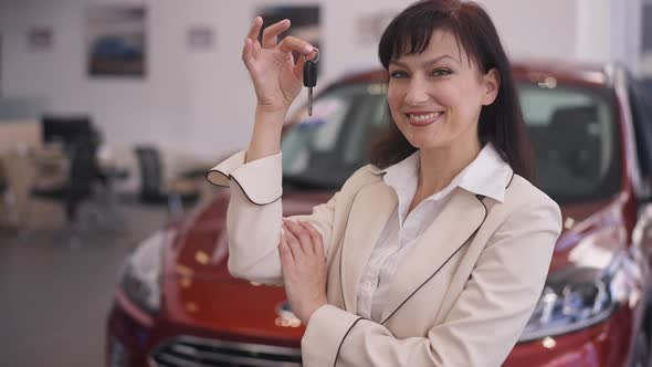 Portrait of Beautiful Caucasian Woman Posing with Car Key in Dealership Smiling Looking at Camera