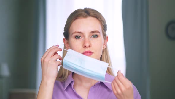 Young attractive girl putting on a medical blue mask at home