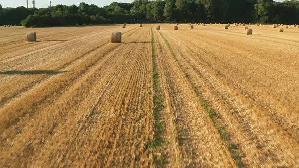 flying forward over a wheat field after harvest with bales of hay