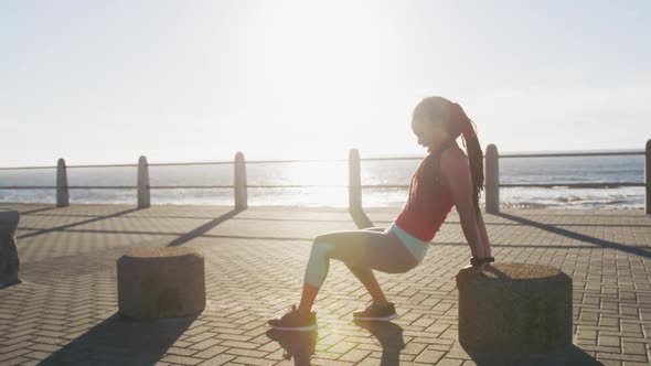 African american woman in sportswear exercising on promenade by the sea