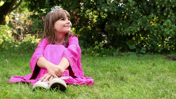 Girl wearing pink dress and tiara sitting on grass