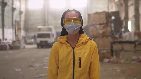 A Positive Girl in Protective Working Clothes Yellow Jacket Eyeglasses and Mask Walking By Recycling