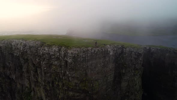 Aerial view of woman standing on the edge of English Slave cliff, Faroe island.