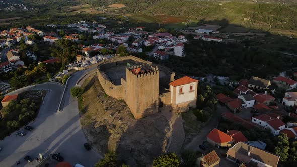 A drone pulls back from the tower at Belmont castle at sunset surrounded by birds.