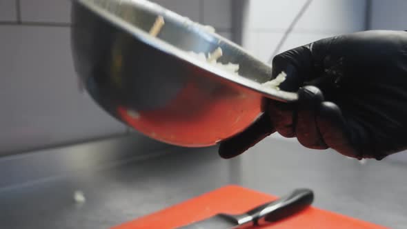 Male Hand of Chef in Glove Tossing Ingredients and Mixing Them in Iron Bowl