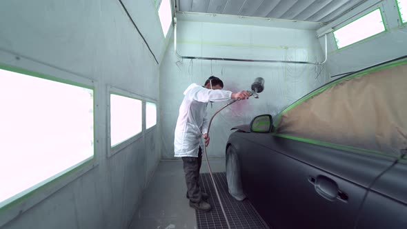 Car body painter spraying car in paint booth