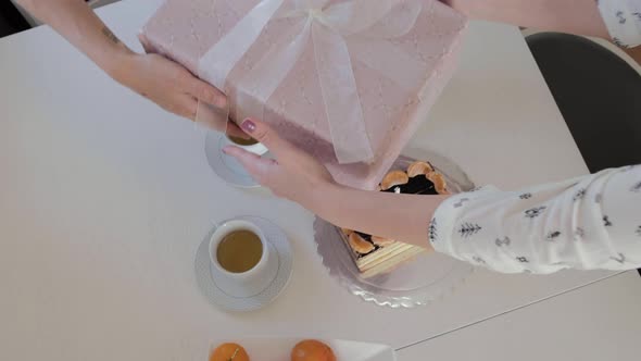 Top view of female hands give a gift in a box on the background of the cake