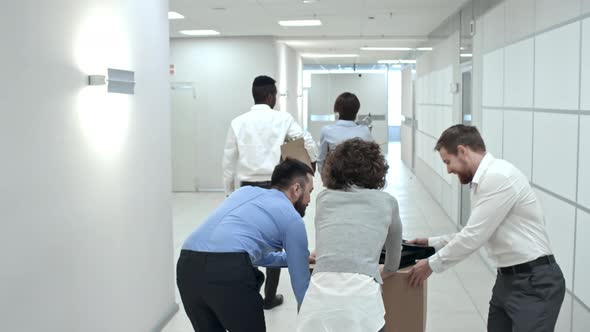 Business Team Pushing Cardboard Box though Office Hallway