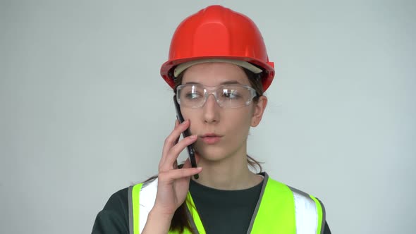 A Beautiful Young Female Construction Worker in a Safety Helmet is on the Phone
