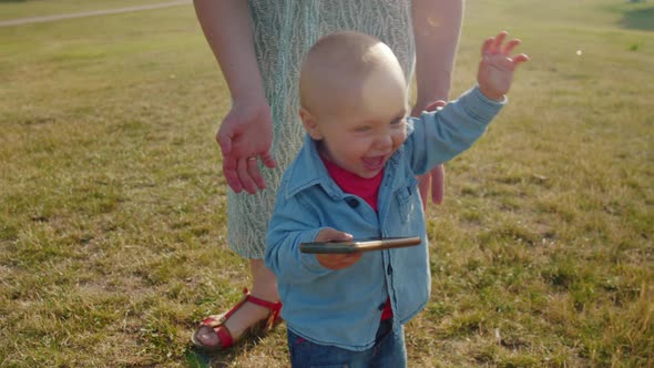 Child Takes the First Steps Walking in the Park with Mom