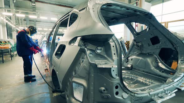 Automobile Factory Worker Is Welding Body of an Unfinished Car