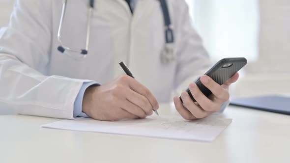 Doctor Writing and Using Smartphone