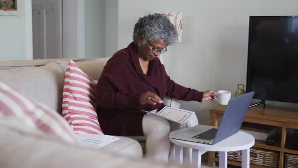 Senior african american woman drinking coffee while calculating finances at home
