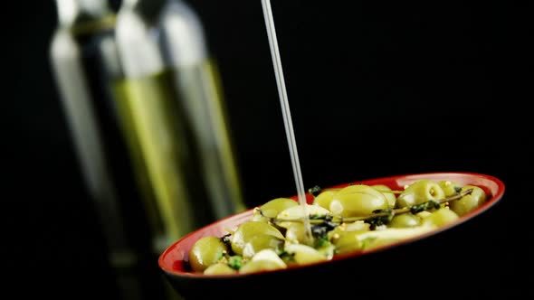 Olive oil being poured in the bowl of green olives with herbs