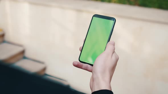 Over the Shoulder Shot of Man Using a Phone with a Green Screen Outdoors. Handsome Man Scrolling