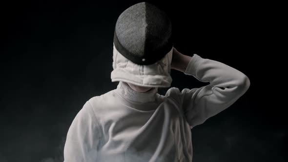 Fencing Training in the Studio - Young Woman Putting on a Helmet and Stands in the Position