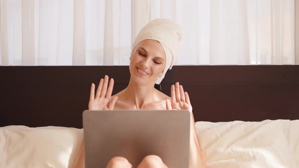 Young Woman in Bath Towel Resting on Cozy Bed and Using Wireless Laptop for