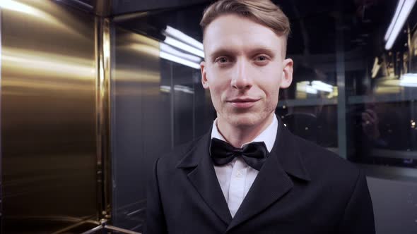 Young Man in a Suit with Bow Tie Rides in the Elevator Looking in the Camera and Smiling