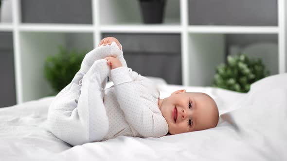 Adorable Baby in Sliders Lying on Bed Playing and Laughing