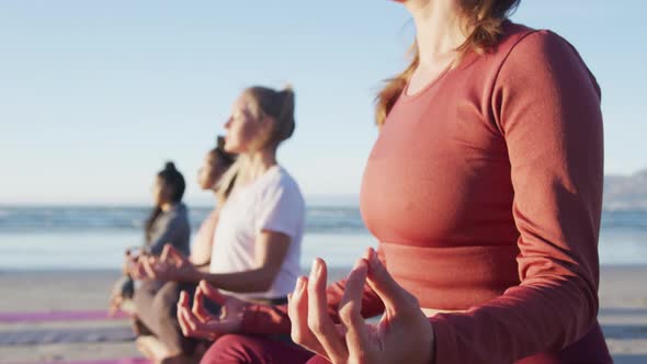 Group of diverse female friends meditating at the beach