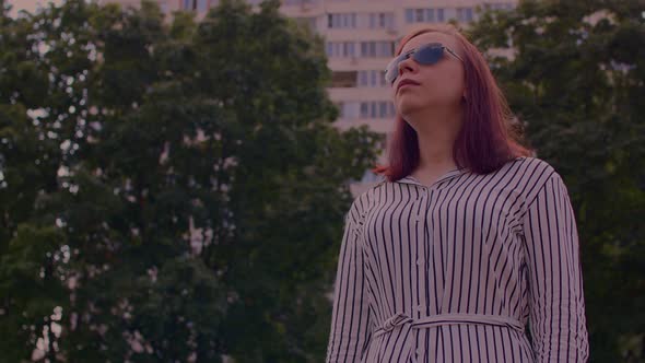 Young Woman in Sunglasses Standing on City Street and Looking Away