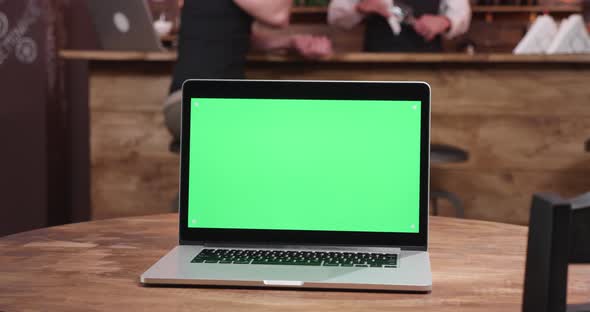 Laptop with Green Screen on the Display in Cozy Cafe