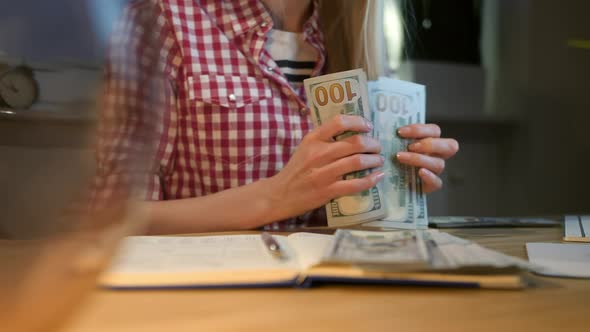 Woman Counting Cash at Working Desk. Attractive Blond Female in Checkered Shirt Sitting at Night in