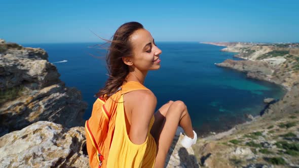 Young Slim Female Traveler Sitting on Cliff Top in Front of Amazing Seascape