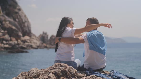 Romantic couple sit and embrace near the sea. Man and woman with black hair spend vacation