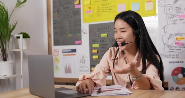 Asian woman with headset using laptop and talking