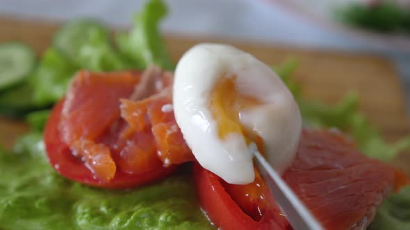 A Poached Egg Is Cut with a Knife on Toast with Poached Egg, Herbs, Salmon and Tomato. Breakfast