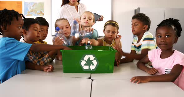 School kids putting waste bottles in recycle bin in classroom