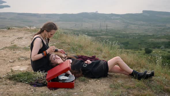 Two Hipster Girls Lie on the Ground in the Mountains and Listen To Music