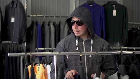 A Man in a Hood and Glasses Steals a T-shirt From a Store. Clothing Store.